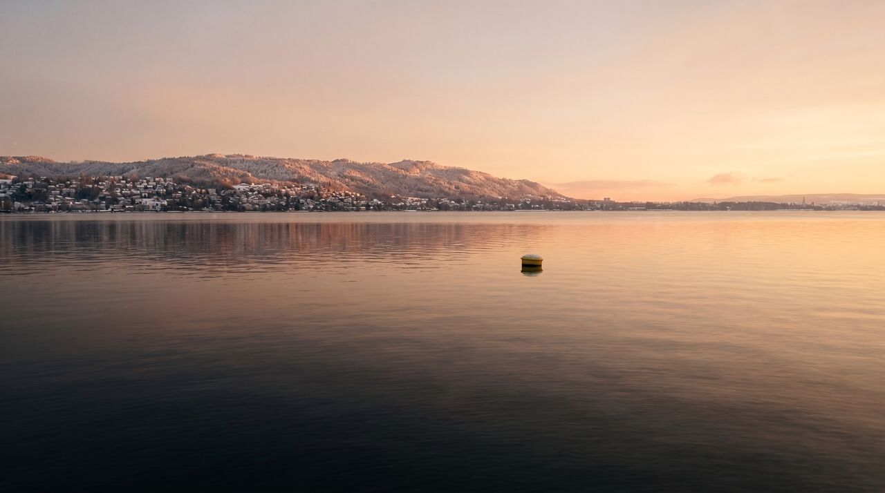 Der Zürichsee an einem Winterabend nach Sonnenuntergang, verschneite Hügel am Gegenufer (Foto, KI-bearbeitet, illustrativ).